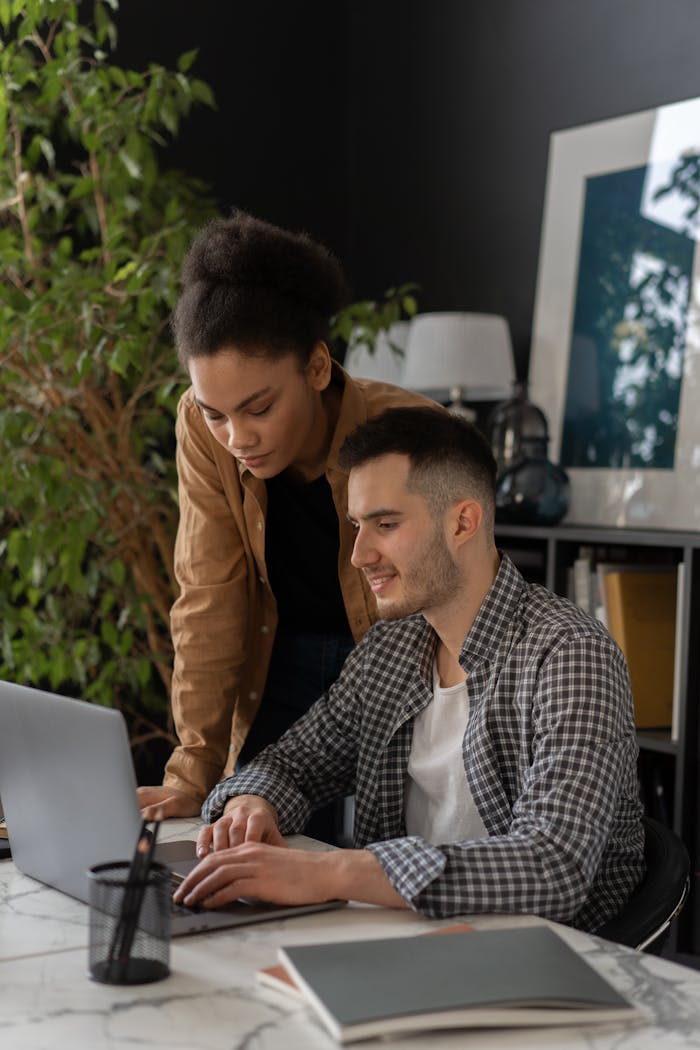Two colleagues work together on a laptop in a modern office setting.